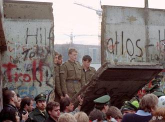 East German border guards look through a hole in the Berlin wall after demonstrators pulled down one segment of the wall at Brandenburg gate in this Nov. 11, 1989 file picture