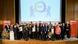 The picture shows a stage on which numerous people (award winners and laudators) are standing and looking happily into the camera. In the background is a screen on which the logo of the Berlin Inclusion Award can be seen.